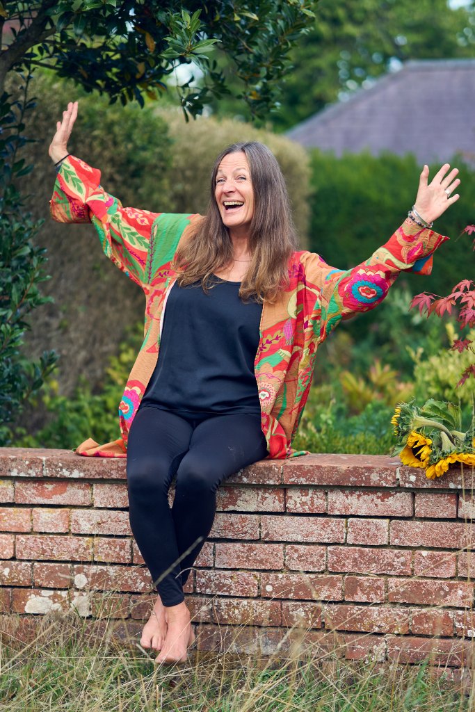 Cat Googe sat on a wall laughing with her hands in the air. 